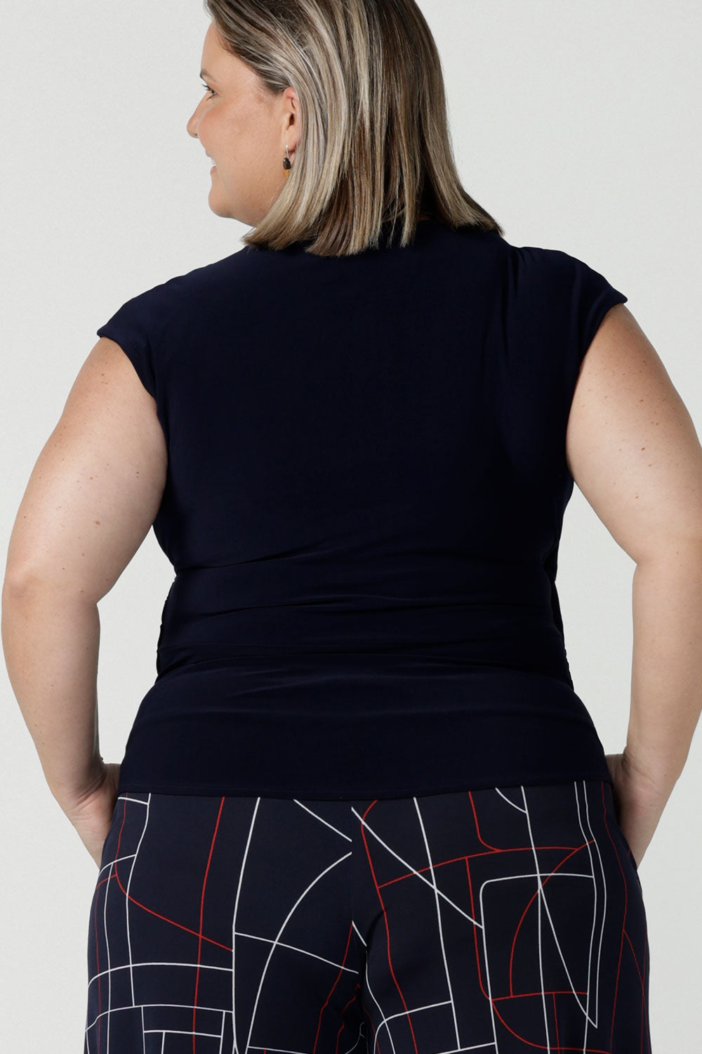 Back view of a size 16 curvy woman wears the Finely top in Navy. A fixed wrap style perfect for corporate to casual wear. Made in Australia for women size 8 - 24.