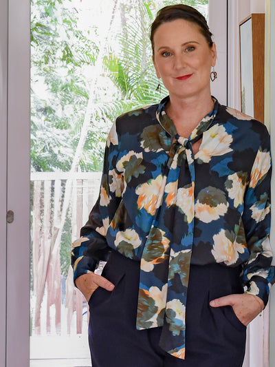 Founder of Australian fashion brand, Leina & Fleur, New Zealand-born Fleur Richardson, wears a pussy bow shirt in floral print sustainable fabric with high-waisted tapered navy work pants. 