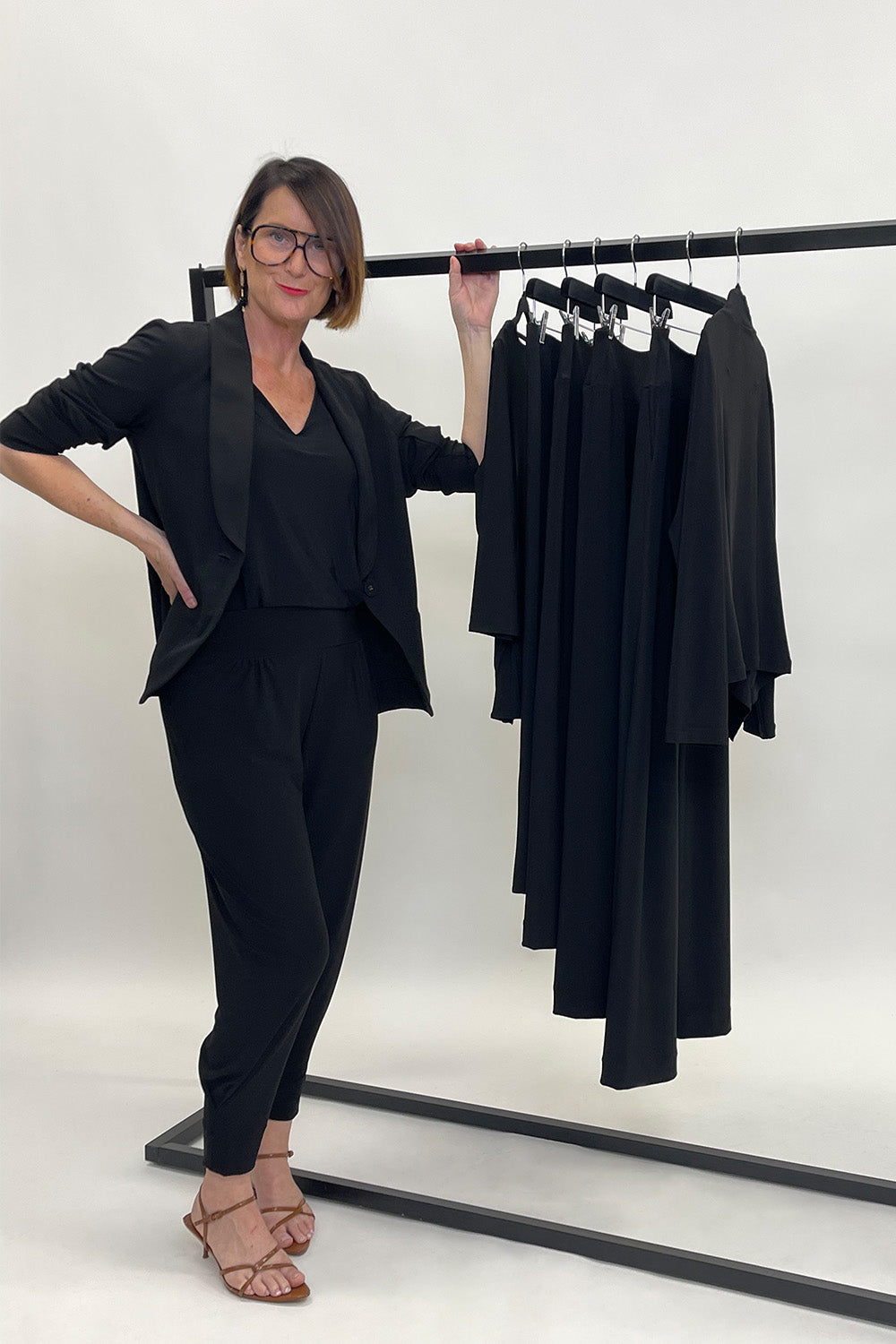 Woman in a black outfit standing next to a rack of black clothing on a white background