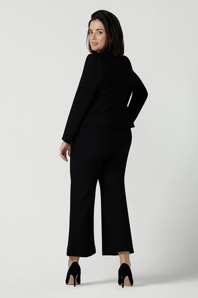 Back view of a Size 10 woman wears the Garcia Jacket in Black. Tailored design with collar and comfortable stretch. Comfortable and stylish workwear for women. Size inclusive fashion and made in Australia for women size 8 - 24. Styled back with Black Kick flare Troy pants, boot leg cut. 