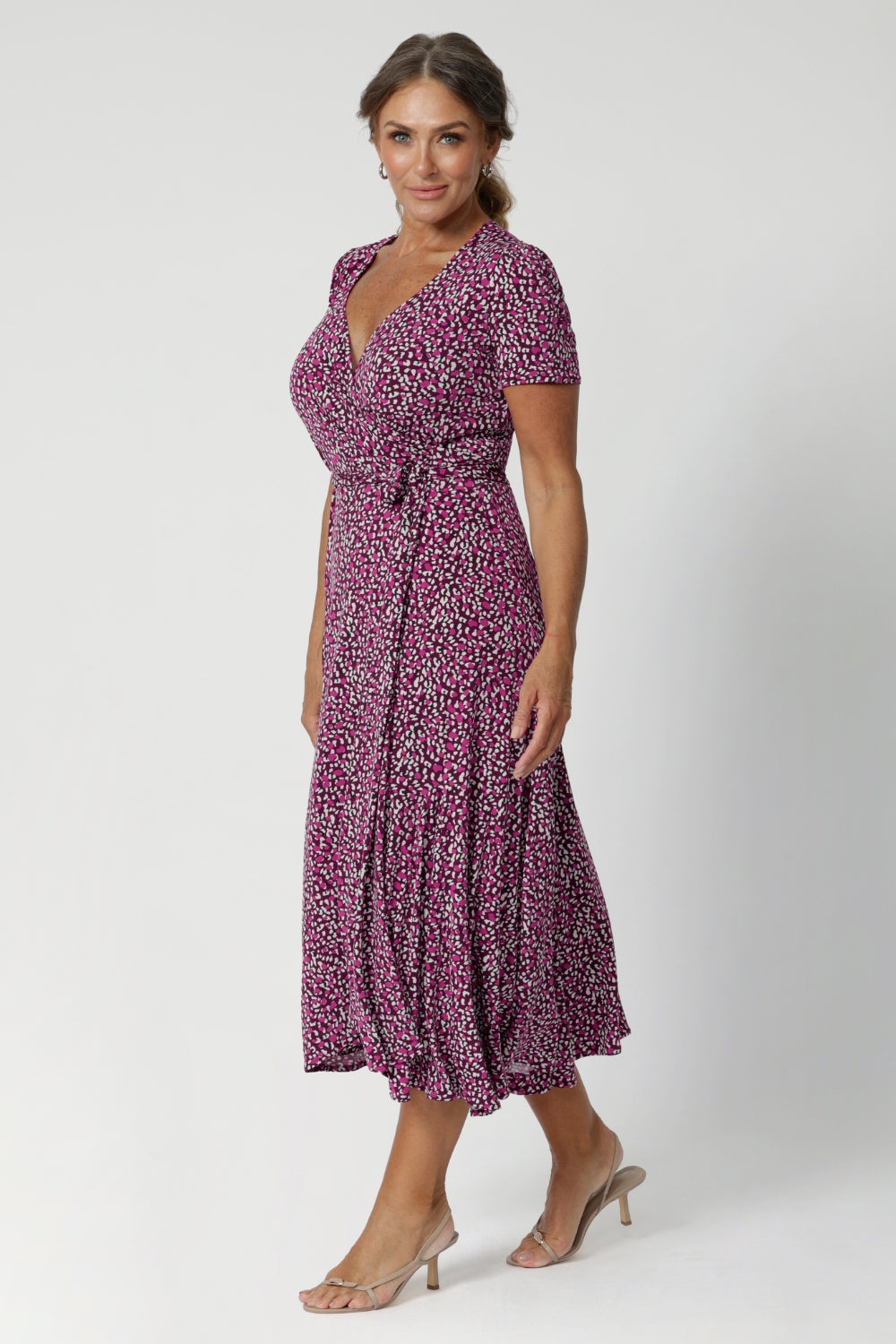 Over 40's woman wears wrap-style dress silhouette, that hugs the body in all the right places while offering a comfortable fit for a wide range of shapes and sizes, from 8 to 24, including petite and plus sizes. Crafted from easy care fabric by Leina & Fleur. 