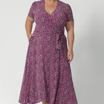 Plus size woman wears printed pink dress with tailored featured including double-layer back bodice for extra support and extended waist ties that allow for an adjustable fit. The short sleeves are beautifully finished with gathering at the sleevehead, giving the dress a fresh, feminine feel. Available in sizes 8-24.