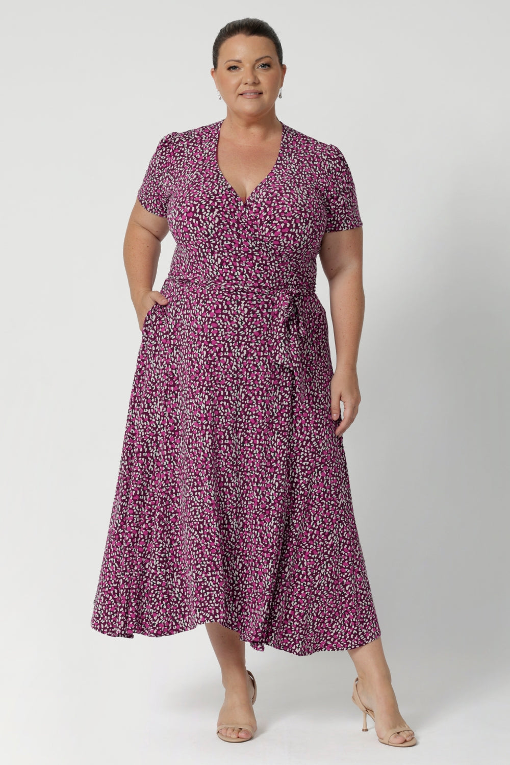 Plus size woman wears printed pink dress with tailored featured including double-layer back bodice for extra support and extended waist ties that allow for an adjustable fit. The short sleeves are beautifully finished with gathering at the sleevehead, giving the dress a fresh, feminine feel. Available in sizes 8-24.