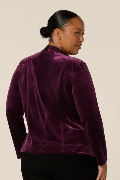 Back view of occasionwear dressing at its finest, this soft tailoring jacket in red wine velour adds effortless glamour to black cocktail wear. Shown here over a black cami top and slim leg black trousers, this open front, soft collared evening jacket is made in Australia in sizes 8 to 24.