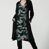 A size 10 model wears the Alpine Fern Heather dress in jersey. Made in Australia for women size 8 - 24. Fern green with leaf print all over. Styled back with the black Sorel Trenchcoat and winter boots. 