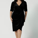 A curvy size 18 model wears the Hedy dress in Black. A velour functioning wrap dress with a tulip skirt and draped front. Up Late evening wear for event dressing. Size inclusive sustainable fashion made in Australia size 8 - 24. 