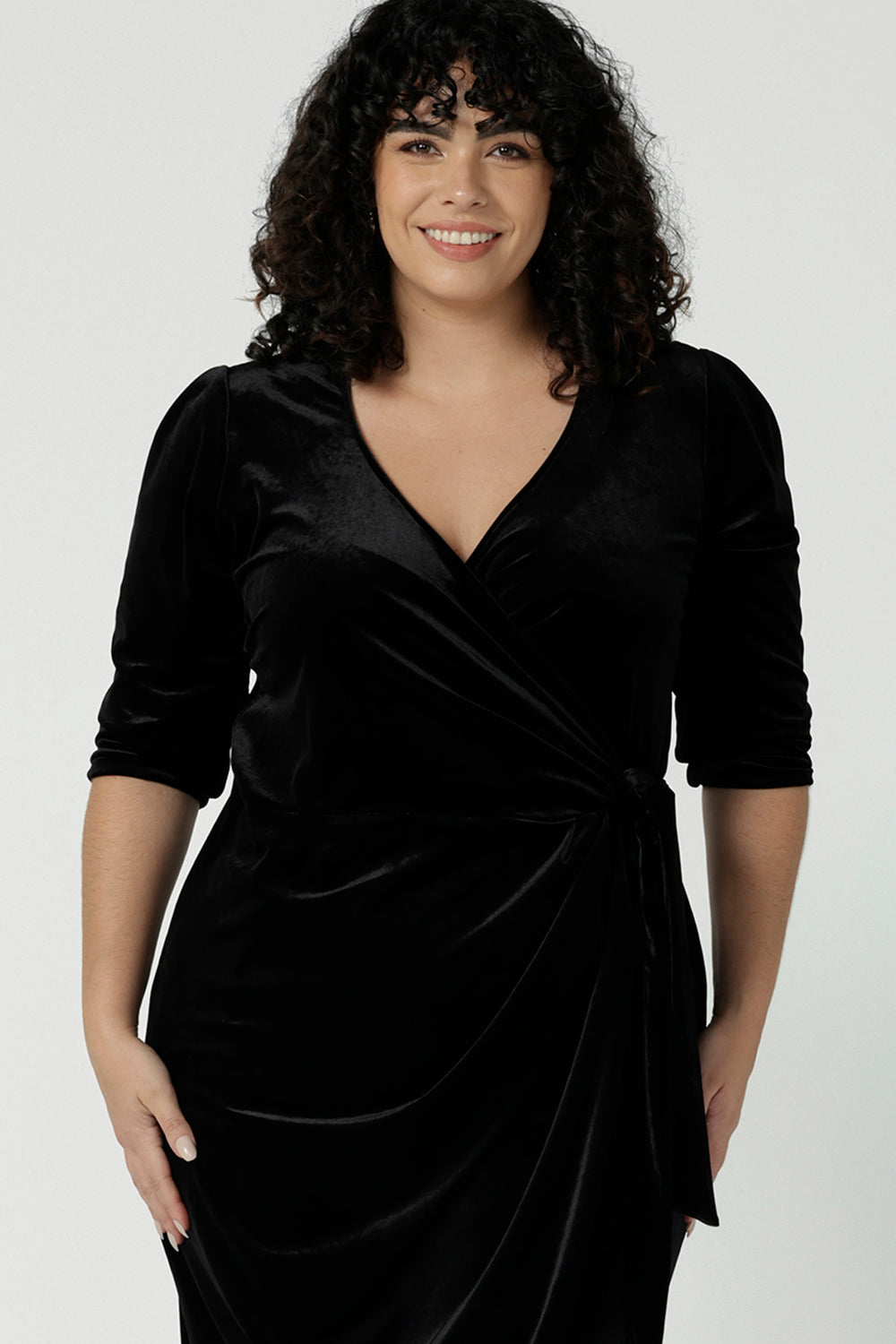 Close up of a curvy size 18 model wears the Hedy dress in Black. A velour functioning wrap dress with a tulip skirt and draped front. Up Late evening wear for event dressing. Size inclusive sustainable fashion made in Australia size 8 - 24.