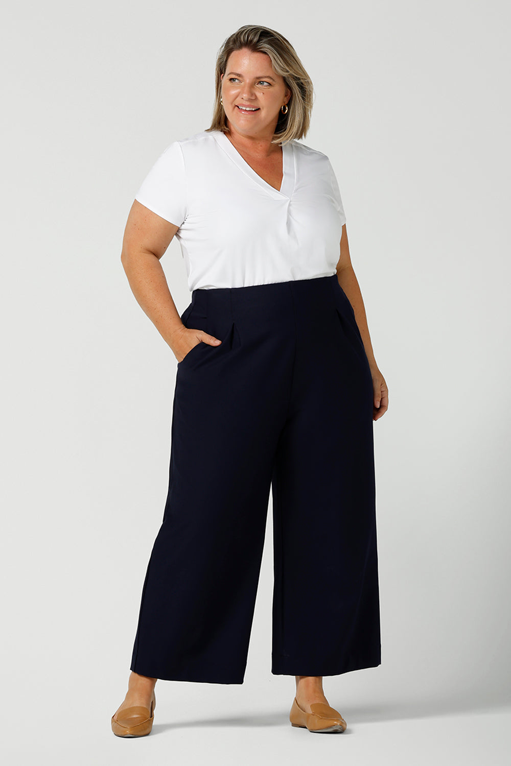 A good top for your capsule wardrobe, this V-neck tailored top in white bamboo jersey has short sleeves and is worn with Navy blue, wide leg culotte pants. Shown on a size 18, curvy woman, this is a great top for plus size office wear. Made in Australia by ethical clothing brand, Leina & Fleur, shop ladies tops in petite to plus sizes online in their online fashion boutique.