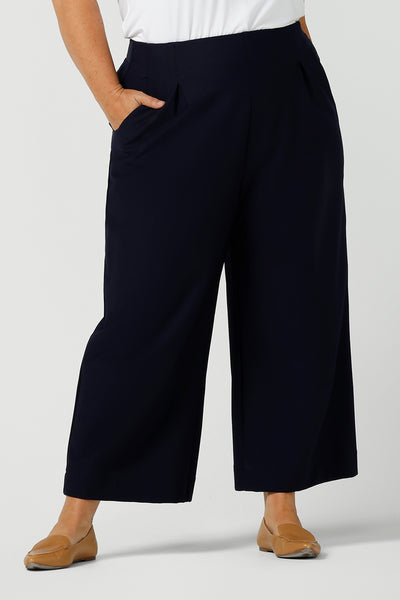 A plus size, size 18 woman wears the wide-leg, cropped length Hollis Culotte Pant in Navy blue. Featuring front pleats, side pockets and stretch jersey fabric these are comfortable, plus size  work pants. This tailored trouser delivers quality office wear to women in sizes 8 to 24. - shop now in Australian women's clothing brand, Leina & Fleur's online boutique.