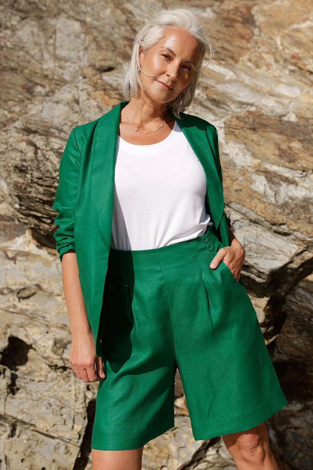 A mature woman wears 100% Linen Bermuda shorts. The perfect smart casual shorts suitable for summer workwear to take you through to the weekend. Styled back with a soft tailored emerald green linen blazer.  Both in a beautiful emerald green colour and soft tailoring details. Designed and made in Australia for sizes 8 -24.