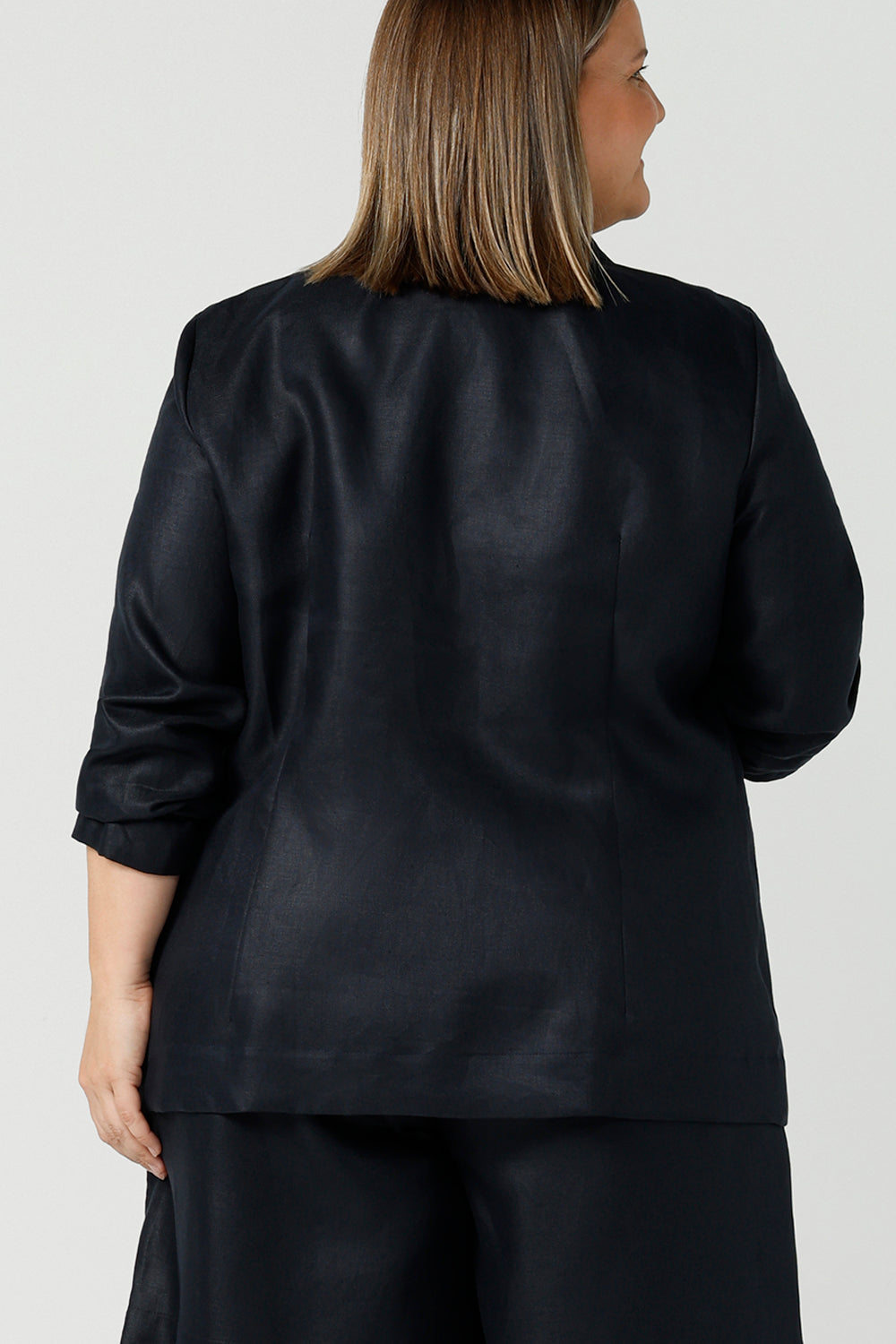 Back view of a size 18 woman wearing a 100% linen blazer jacket with a tailored design. Breathable linen fabric. This blazer has a relaxed fit a button front construction. A transeasonal linen work jacket, in a luxe midnight navy colour. Australian-made using sustainable 100% linen fabric. Size-inclusive fashion 8-24 for corporate casual workwear.