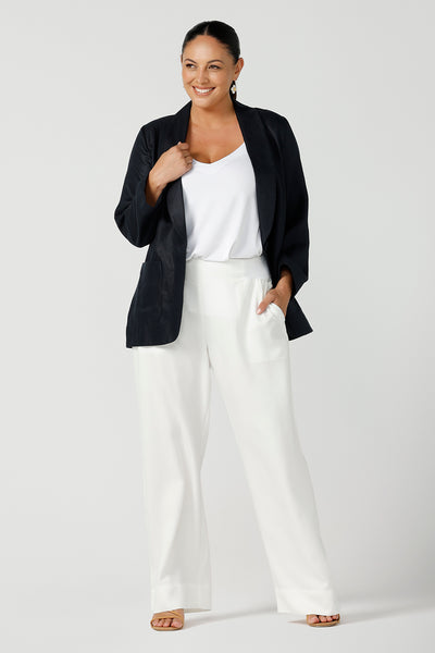A size 12 woman wearing a soft linen blazer jacket with a tailored design. A transeasonal linen work jacket, in a beautiful midnight navy colour. Australian-made using sustainable 100% linen fabric. Styled back with white pants and a white babmoo cami top. Size-inclusive fashion 8-24 for corporate casual workwear.