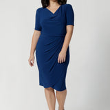 The cowl neckline adds a touch of sophistication and elegance to the design, while the elbow-length sleeves with tuck details at the shoulder provide a unique, refined look. Available in sizes 8-24. Petite height model wears Imelda Dress in Blue  with platform dress.