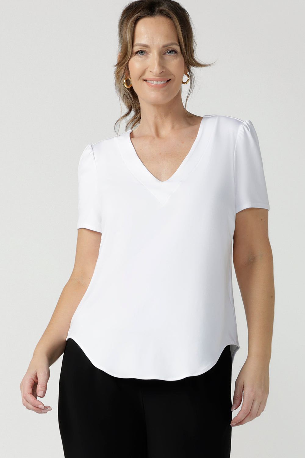A size 10, 40 plus woman wears a V-neck, short sleeve top in white bamboo jersey. This tailored white top cuts a T-shirt look for casual wear and comfortable workwear. Shop made-in-Australia bamboo jersey tops online in petite, mid size and plus sizes at women's clothing brand, Leina & Fleur.