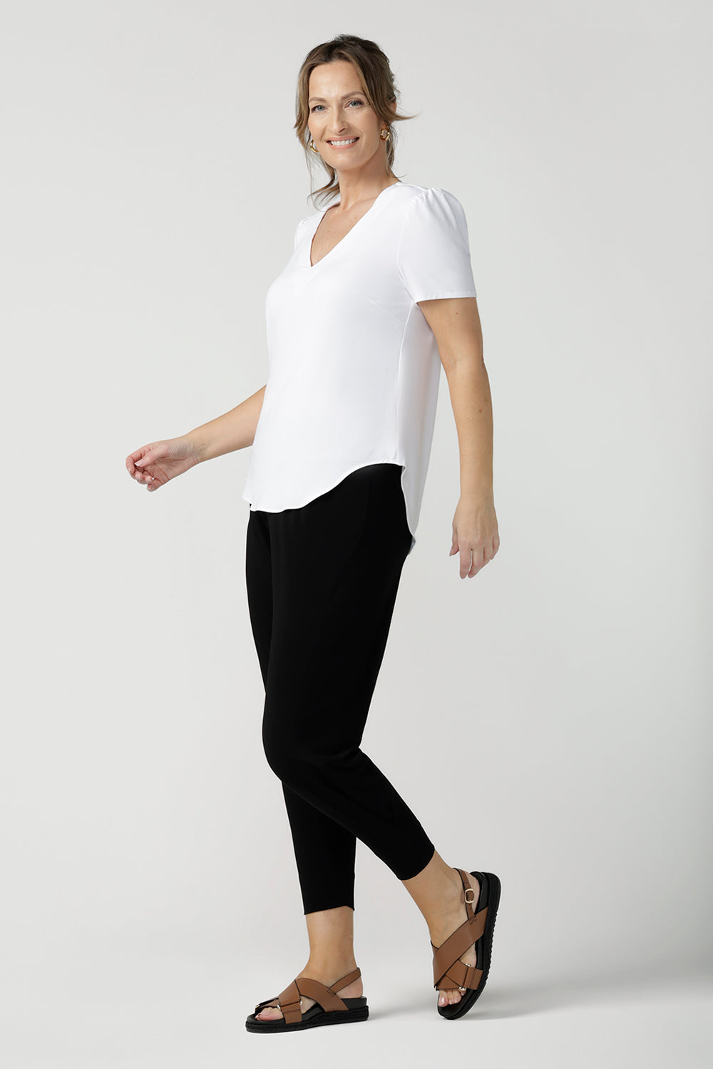 Side view of a size 10, 40 plus woman wears a V-neck, short sleeve top in white bamboo jersey with tapered leg, cropped jersey travel pants. This tailored white top cuts a T-shirt look for casual wear and comfortable workwear. Shop made-in-Australia bamboo jersey tops online in petite, mid size and plus sizes at women's clothing brand, Leina & Fleur.