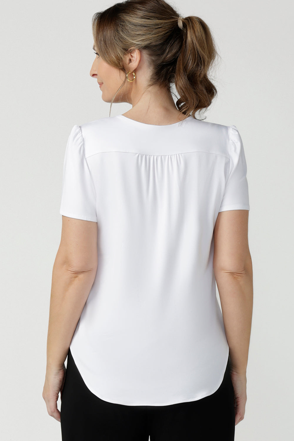 Back view of size 10, 40 plus woman wears a V-neck, short sleeve top in white bamboo jersey. This tailored white top cuts a T-shirt look for casual wear and comfortable workwear. Shop made-in-Australia bamboo jersey tops online in petite, mid size and plus sizes at women's clothing brand, Leina & Fleur.