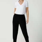 A size 10, 40 plus woman wears a V-neck, short sleeve top in white bamboo jersey with tapered leg, cropped jersey travel pants. This tailored white top cuts a T-shirt look for casual wear and comfortable workwear. Shop made-in-Australia bamboo jersey tops online in petite, mid size and plus sizes at women's clothing brand, Leina & Fleur.