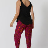 Back view of over 40 year old woman wearing Indi pants in paisley print featuring colours of fuchsia and tangerine. Drop crotch feature provide extreme comfort for busy days and travel adventures. Bold colour way can be styled casually or dressed up for the season.