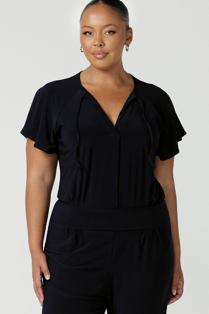 A plus size, size 18 woman wears a casual jersey top in navy blue. This Australian-made women's top has short raglan sleeves, a V-neckline and and shirttail hem - perfect for weekend casual and travel capsule wardrobes. 