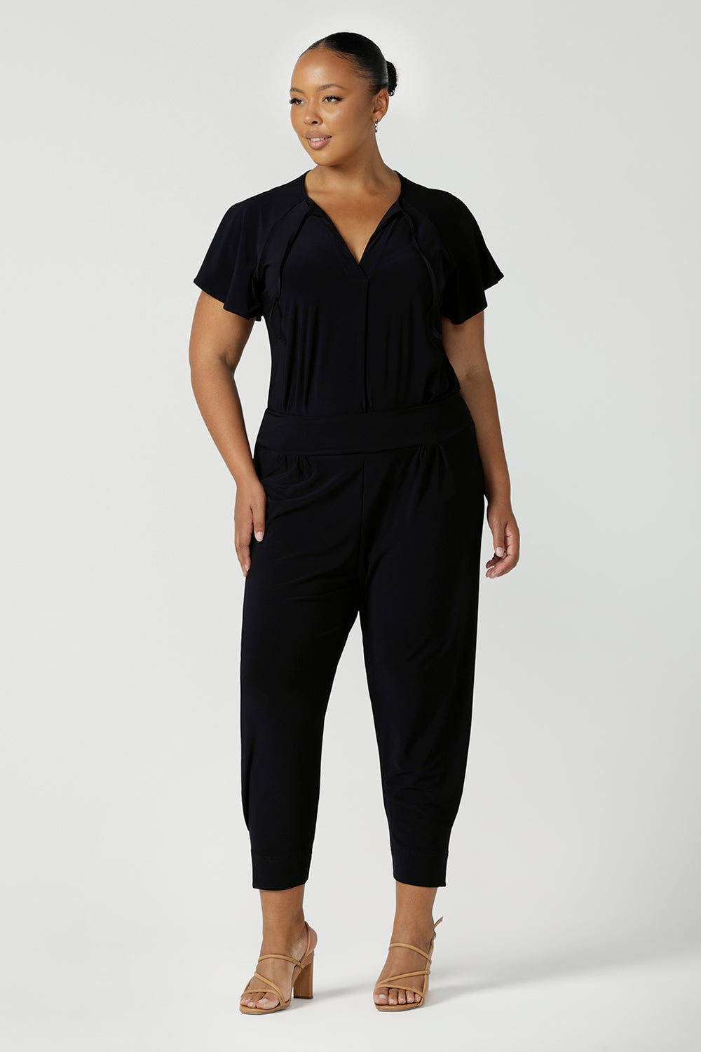 A plus size, size 18 woman wears a casual jersey top in navy blue. Worn with dropped crotch travel pants in navy blue,  this Australian-made women's top has short raglan sleeves, a V-neckline and a shirttail hem - perfect for weekend casual and travel capsule wardrobes. 