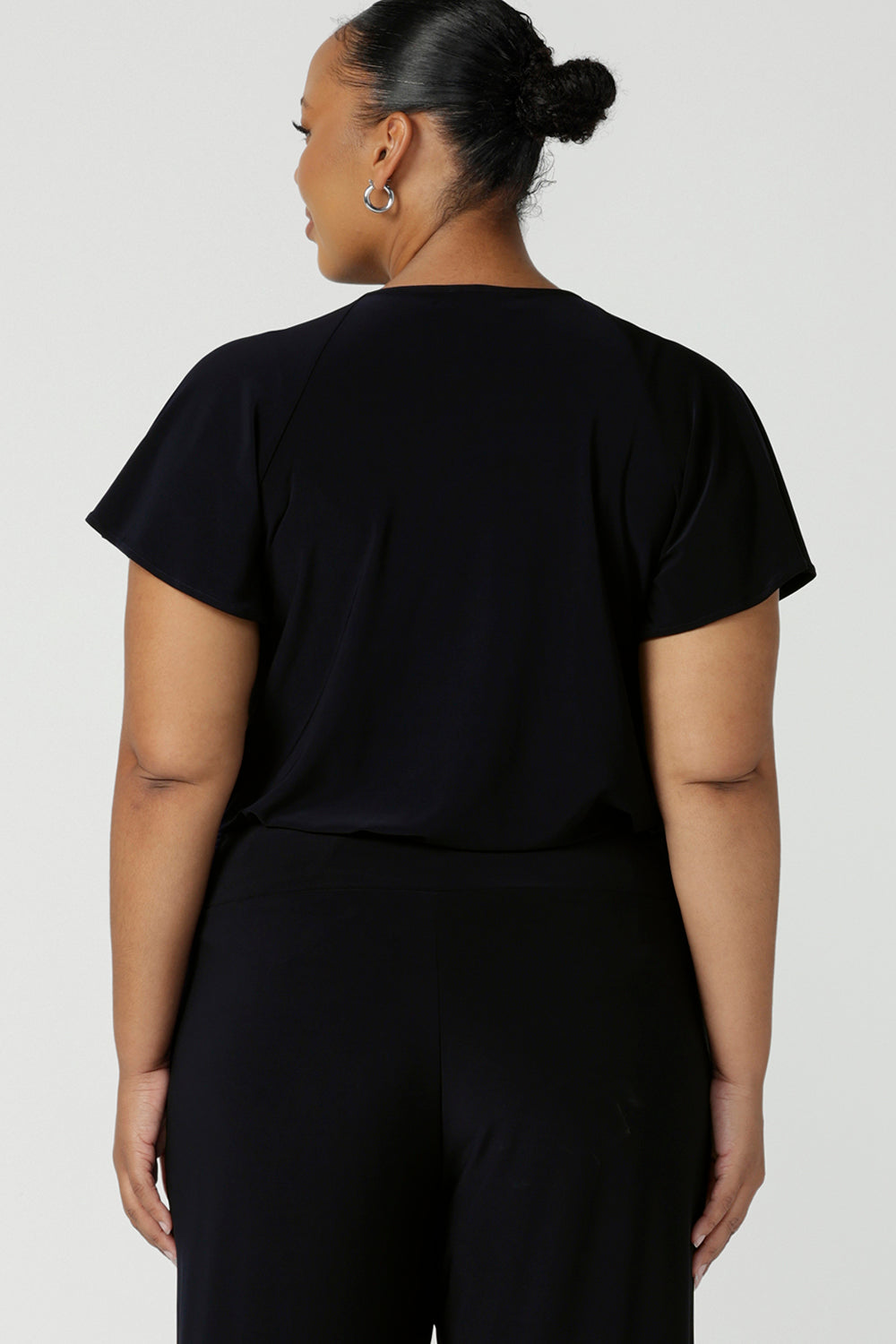 Back view of a plus size, size 18 woman wears a casual jersey top in navy blue. This Australian-made women's top has short raglan sleeves, a V-neckline and and shirttail hem - perfect for weekend casual and travel capsule wardrobes. 