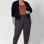 The tapered leg shape is flattering, and the ankle cuffs with tuck detail provide a polished finish. With a 7/8 length, these pants are versatile enough to be dressed up or down, making them a must-have for travel, work, or casual outings. Whether you're on the go or looking for a chic and comfy addition to your wardrobe, the Indi pant is the perfect choice. Size 18 woman wears printed pants with clay cami and navy cardigan. 