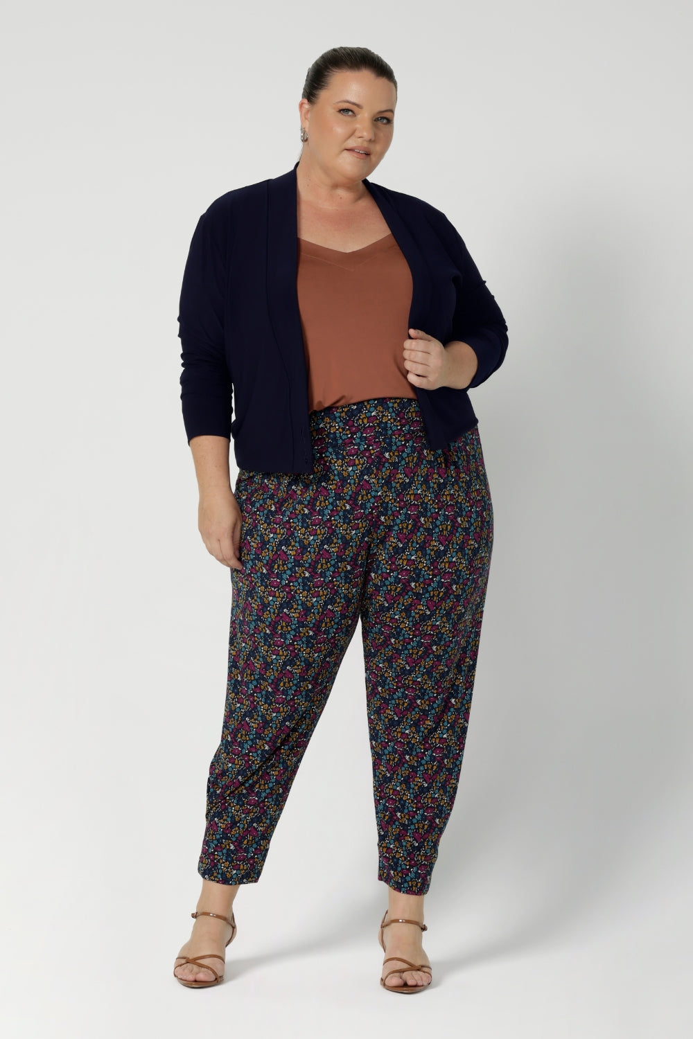 The tapered leg shape is flattering, and the ankle cuffs with tuck detail provide a polished finish. With a 7/8 length, these pants are versatile enough to be dressed up or down, making them a must-have for travel, work, or casual outings. Whether you're on the go or looking for a chic and comfy addition to your wardrobe, the Indi pant is the perfect choice. Size 18 woman wears printed pants with clay cami and navy cardigan. 