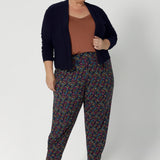 The tapered leg shape is flattering, and the ankle cuffs with tuck detail provide a polished finish. With a 7/8 length, these pants are versatile enough to be dressed up or down, making them a must-have for travel, work, or casual outings. Whether you're on the go or looking for a chic and comfy addition to your wardrobe, the Indi pant is the perfect choice. Size 18 woman wears printed pants with clay cami and navy cardigan. 