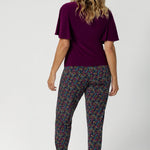 Over 40's women wears long length, pull on style pant, featuring tapered leg and floral print. Travel ready pant is made of light weight dry touch jersey - that is wrinkle resistant and cooling.