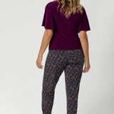 Over 40's women wears long length, pull on style pant, featuring tapered leg and floral print. Travel ready pant is made of light weight dry touch jersey - that is wrinkle resistant and cooling.