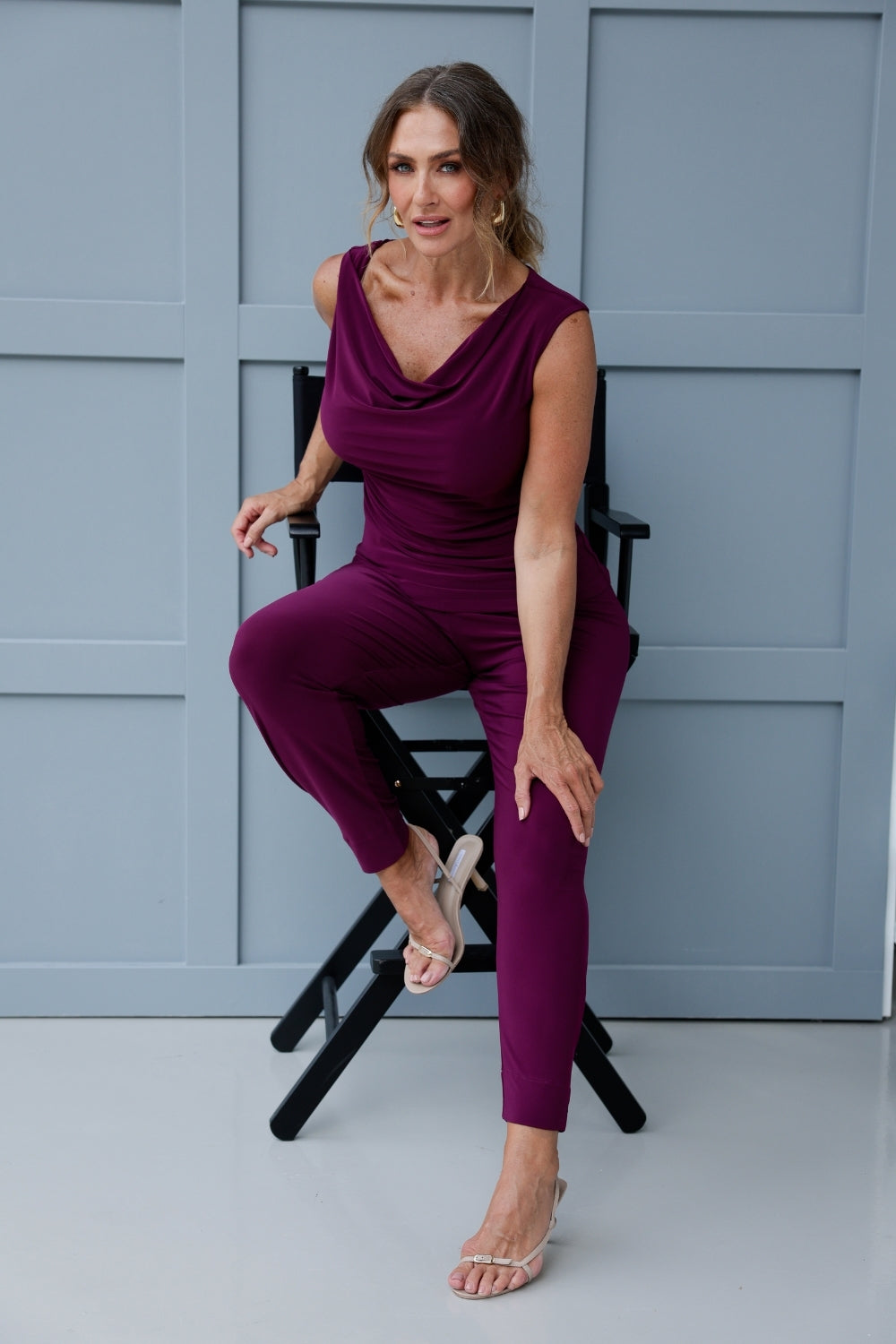 Indi is a stylish and ultra-comfortable pant that’s perfect for both travel and everyday wear. In a vibrant magenta hue, these pants effortlessly combine comfort with modern design, making them a go-to wardrobe staple you'll want in more than one pair. 40 year old woman wears magenta coloured pants with matching cowl neck top, creating a jumpsuit look.