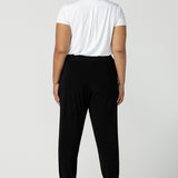 Back view of a size 18 curvy woman wears great pants for travel, these dropped crotch, single seam black pants are made stretchy jersey for ultimate comfort. Worn with a white bamboo jersey top , shop these comfy black pants for your travel and capsule wardrobe now!