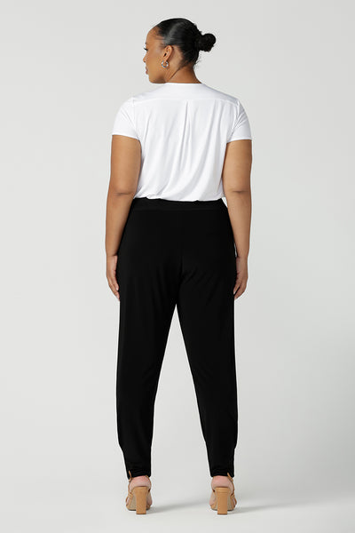 Back view of a size 18 curvy woman wears great pants for travel, these dropped crotch, single seam black pants are made stretchy jersey for ultimate comfort. Worn with a white bamboo jersey top , shop these comfy black pants for your travel and capsule wardrobe now!