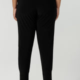 Back view of a size 18 curvy woman wears great pants for travel, these dropped crotch, single seam black pants are made stretchy jersey for ultimate comfort. Worn with a white bamboo jersey top , shop these comfy black pants for your travel and capsule wardrobe now!