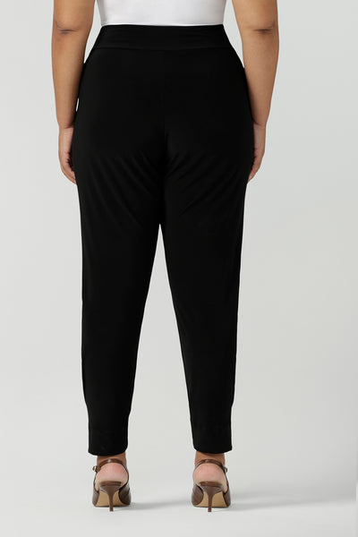 Back view of a size 18 curvy woman wears great pants for travel, these dropped crotch, single seam black pants are made stretchy jersey for ultimate comfort. Worn with a white bamboo jersey top , shop these comfy black pants for your travel and capsule wardrobe now!