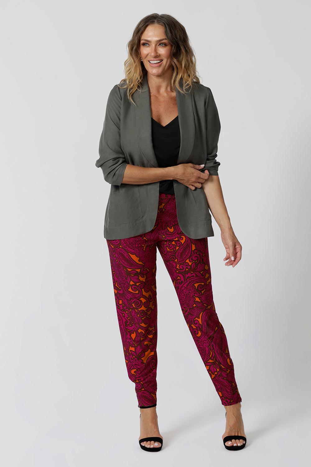 Travel ready pant featuring fuchsia & tangerine colours worn by over 40 year old woman showcases pants styled back with black top, black heels and fern coloured blazer for an elevated look. Showcasing versatility in the Indi Tall Pants. Bold paisley colour way can be styled casually or dressy. Women's clothing brand Leina & Fleur stock these pants in sizes 8-24.