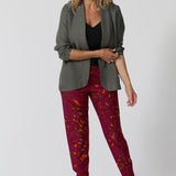 Travel ready pant featuring fuchsia & tangerine colours worn by over 40 year old woman showcases pants styled back with black top, black heels and fern coloured blazer for an elevated look. Showcasing versatility in the Indi Tall Pants. Bold paisley colour way can be styled casually or dressy. Women's clothing brand Leina & Fleur stock these pants in sizes 8-24.