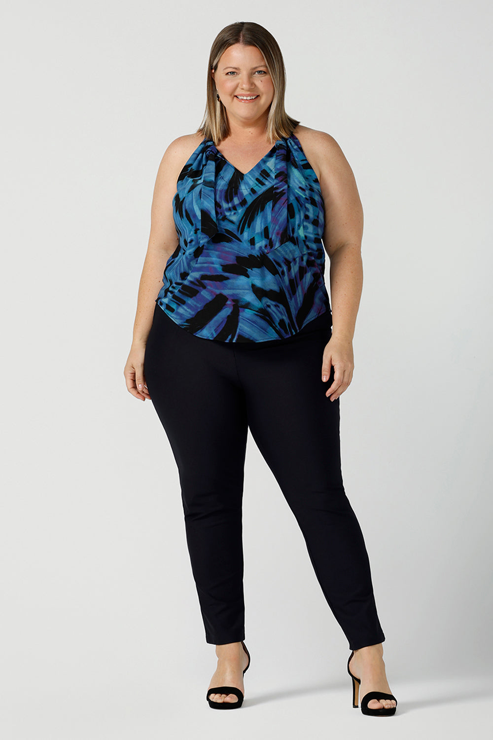 Curvy woman wearing a size 18 tie neck tie top Iris in Flutter with a blue digital print. Size inclusive clothes for women size 8 - 24. Digital blue and purple print. Made in Australia. Styled back with navy slim fit Brooklyn pant.