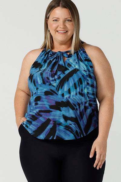 Curvy woman wearing a size 18 tie neck tie top Iris in Flutter with a blue digital print. Size inclusive clothes for women size 8 - 24. Digital blue and purple print. Made in Australia. Styled back with navy slim fit Brooklyn pant.