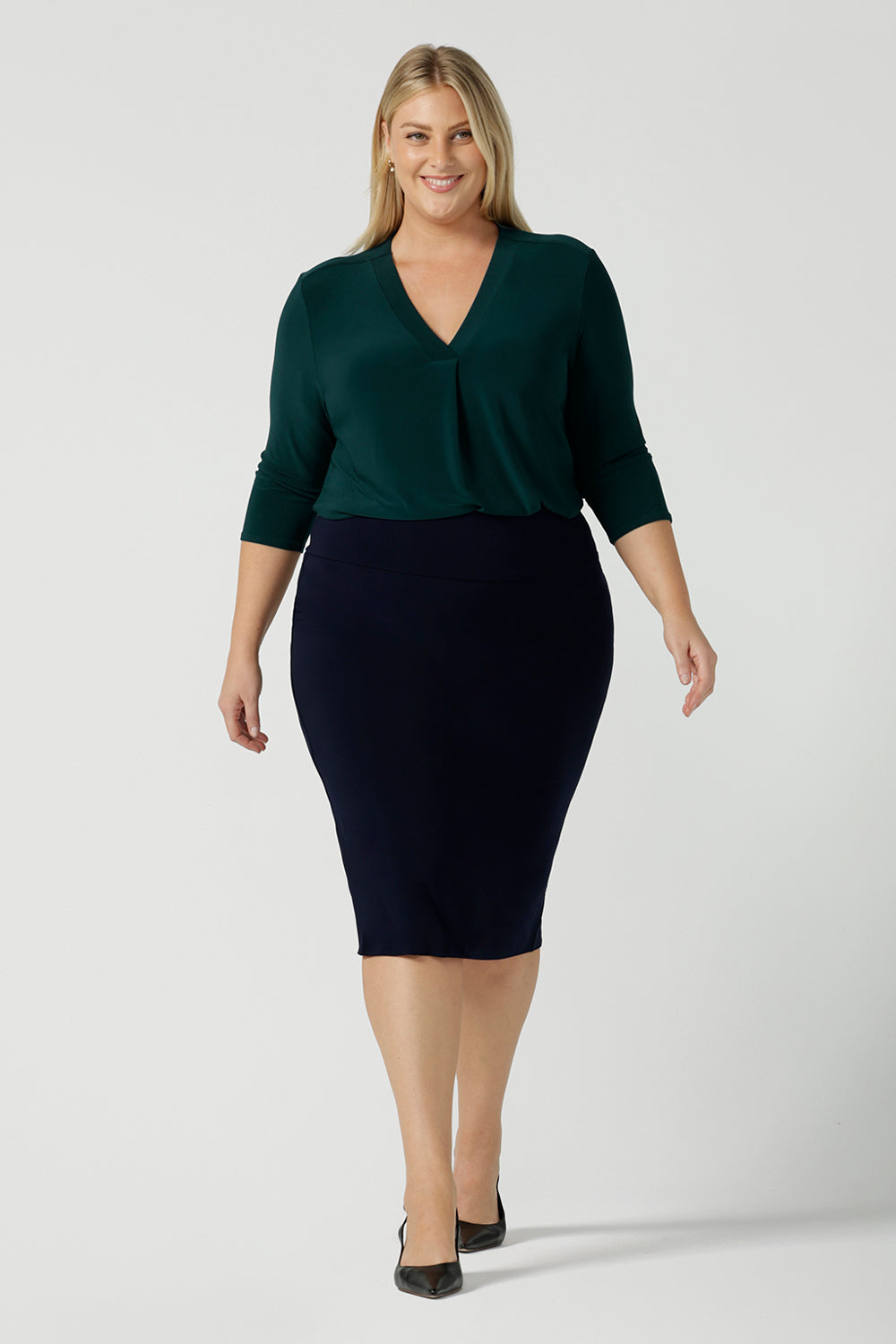 A size 18 woman wears the Jaime Top in Alpine with a soft pleated neckline and 3/4 sleeves. A fitted Andi skirt in Navy. Easy care jersey that is perfect for work to weekend. Made in Australia for women size 8 - 24. Styled back with black sling back pumps. 