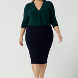 A size 18 woman wears the Jaime Top in Alpine with a soft pleated neckline and 3/4 sleeves. A fitted Andi skirt in Navy. Easy care jersey that is perfect for work to weekend. Made in Australia for women size 8 - 24. Styled back with black sling back pumps. 