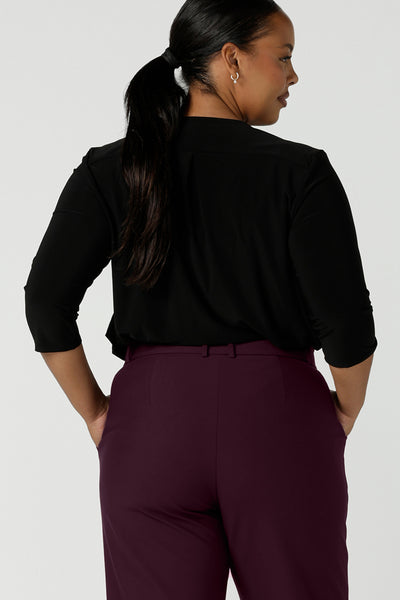 Back view of a size 16 curvy woman wears the Jaime top in black. A comfortable corporate work top with soft tailoring elements like a pleat front neckline, V-neck and 3/4 sleeve. Made in Australia for women size 8 - 24.