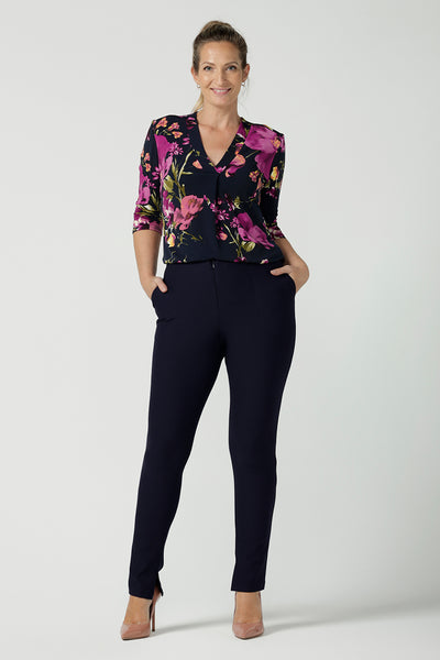 A size 10 woman wears the Jaime Top in Celeste. A comfortable workwear top that is easy care jersey. Featuring 3/4 sleeves and a v-neckline. Made in Australia and size inclusive. Size 8 - 24. Styled back with the Navy Brooklyn pants.