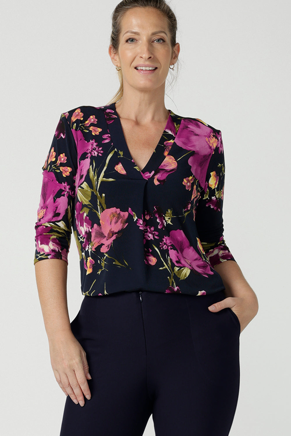 A size 10 woman wears the Jaime Top in Celeste. A comfortable workwear top that is easy care jersey. Featuring 3/4 sleeves and a v-neckline. Made in Australia and size inclusive. Size 8 - 24. Styled back with the Navy Brooklyn pants.