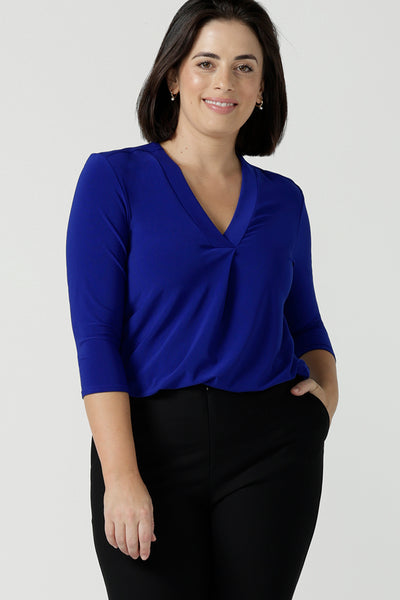 Size 10 Woman wears the Jaime top in Cobalt, a v-neck pleat front top with 3/4 sleeves. Soft Cobalt blue jersey and styled back with black work pants. Made in Australia for women size 8 - 24.  