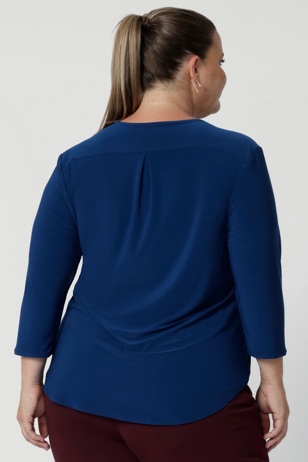 Crafted from a luxurious deep blue dry-touch jersey fabric, this top offers a soft stretch that provides all-day comfort while maintaining a polished, structured look. Plus size woman wears her blue workwear  top in size 18 with wine coloured pants. 