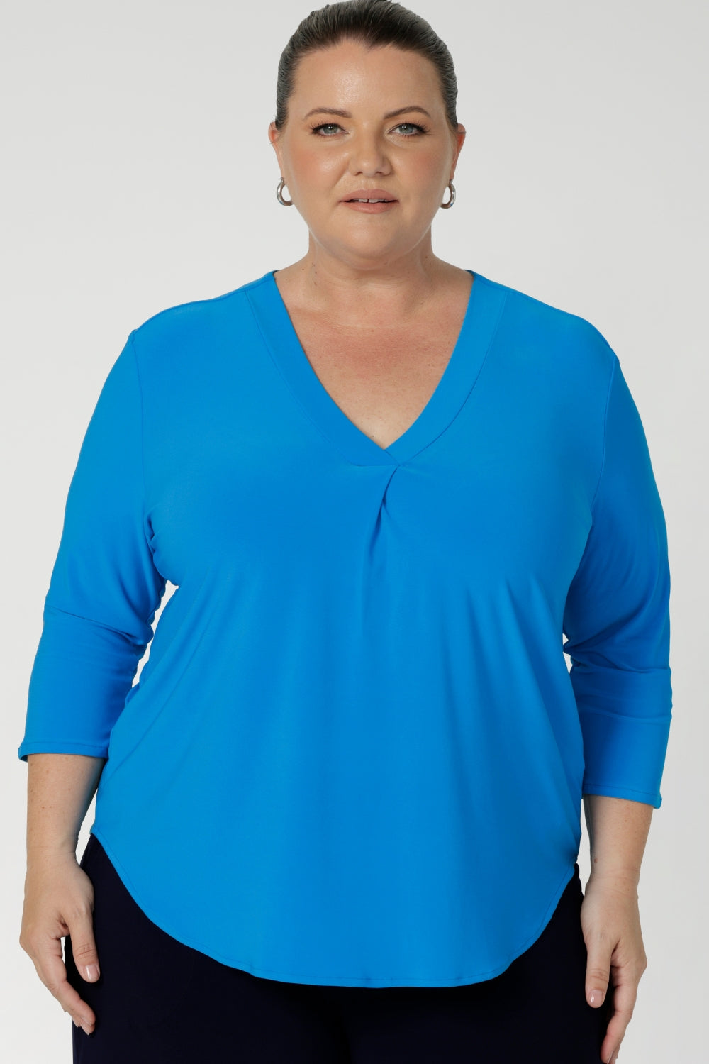 The V-neckline is elevated with a tailored tuck at the center front, adding structure and a refined touch to the design. The 3/4 length sleeves offer just the right amount of coverage, while maintaining a sleek and contemporary look. A center back tailored tuck further enhances the top's polished, tailored appearance, ensuring a flattering shape and clean lines. Size 18 model wears navy pants, matched with opal coloured shirt and silver jewellery.  