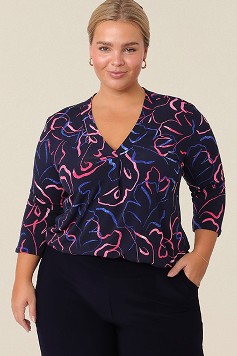 A curvy size 14 woman wears a jersey, V-neck top with 3/4 sleeves. Made-in Australia, this tailored top for work and corporate wear is available in an inclusive 8-24 size range.
