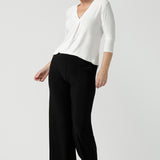 A size 10 woman wears the Jaime top in Vanilla. A comfortable workwear top for women in soft dry touch easy care versey. Featuring a v-neck with pleat front and bind. 3/4 sleeve and made in Australia for women size 8 - 24. Styled back with Black Monroe pants. 