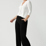 A size 10 woman wears the Jaime top in Vanilla. A comfortable workwear top for women in soft dry touch easy care versey. Featuring a v-neck with pleat front and bind. 3/4 sleeve and made in Australia for women size 8 - 24. Styled back with Black Monroe pants.